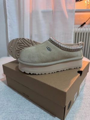 Beige UGG boots med plattform - Säljer ett par beige UGG boots med plattformssula och rund tå. Skorna har ett stickat mönster runt öppningen och är fodrade med mjuk päls på insidan. Utsidan är i mocka och de har en rejäl, räfflad sula som ger bra grepp. Perfekta för kalla dagar.