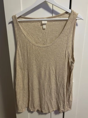 Beige ribbad linnetopp från H&M - Säljer en enkel och stilren beige linnetopp från H&M Basics i storlek M. Toppen är ribbad och har en rund halsringning samt ärmlös design. Väldigt mjukt material