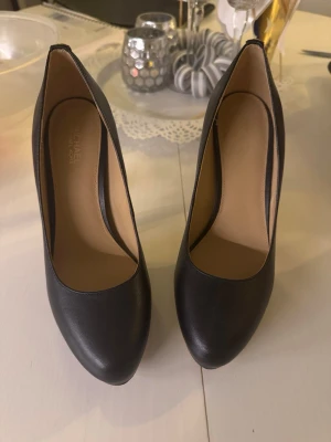 Svarta pumps från Michael Kors - Klassiska svarta pumps från Michael Kors i skinn med rund tå och hög klack. Snygg och stilren design med diskret gulddetalj bak på hälen. 6,5 m motsvarar 37 i storlek. 