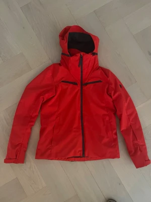 Skidjacka från Peak Performance , dam L - Snygg röd skidjacka från Peak Performance med huva och svarta detaljer. Jackan har mycket bra skick och inga defekter. 
