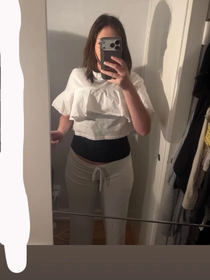 Vit croppad blus med volang - Säljer en vit croppad blus med bred volang över bröstet och ärmarna. Toppen har en lös passform och är tillverkad i ett lätt bomullstyg. Perfekt för dig som gillar en luftig och trendig stil.