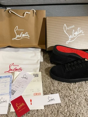 Svarta sneakers från Christian Louboutin - Säljer ett par svarta sneakers från Christian Louboutin med klassisk röd sula. Skorna har rund tå, snörning och är tillverkade i mocka med detaljer i skinn. Snygg och stilren design som sticker ut med den ikoniska röda undersidan.