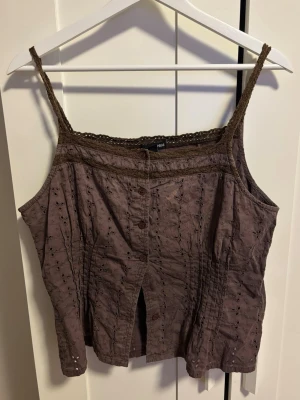 Brun broderad linnetopp från H&M - Säljer en brun linnetopp från H&M i storlek 46. Toppen har tunna axelband, dekorativ spetskant upptill och knappar framtill. Materialet är broderat med små blommor.