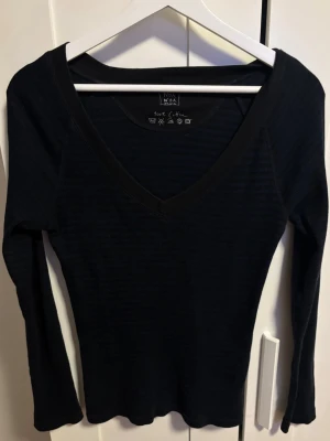 Svart ribbad långärmad topp Noa Noa - Säljer en svart långärmad topp från Noa Noa med diskret ribbad struktur och v-ringad hals. Det är svårt att se på bild med tröjan är randig med mörkblå och svart färg! Tillverkad i 100% bomull vilket gör den mjuk och skön. Står inte storlek men skulle säga runt M.