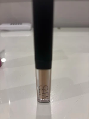 NARS Radiant Creamy Concealer - En concealer från NARS i en ljus beige nyans. Kommer i en stilren, genomskinlig tub med svart lock och applikator. Perfekt för att täcka mörka ringar och ojämnheter. Ger en naturlig finish och är enkel att applicera.