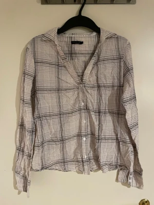 Rutig skjorta från Stockh LM - Luftig och tunn rutig skjorta från Stockh LM i storlek 44. Skjortan har ljusa toner med svart och lila rutmönster, klassisk krage och knäppning framtill. Långärmad och perfekt för en chill och avslappnad stil.