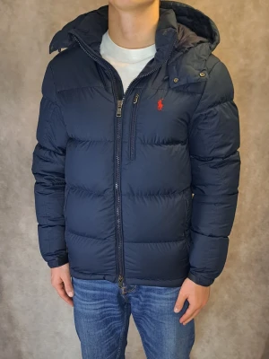 Ralph Lauren Dunjacka - Stl S - 🗻 Riktigt snygg Och Populär Ralph Lauren Dunjacka I Färgen Marinblå! 🗻 Mycket bra skick: 9/10, bara ena spän bandet är sönder ( se bilden), annars är den i nytt skick! Modellen är 175cm lång och sitter riktigt bra! Rekommenderar att vara mellan 168-180cm lång för att sitta fint! Och självklart äkta! 🤝🙌