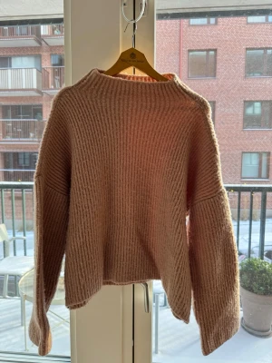 Ljusrosa tröja med breda ärmar - Mysig rosa ribbstickad tröja med breda, långa ärmar och halvhög hals. Tröjan har en loose passform och är tillverkad i en mjuk blandning av akryl och polyester. 🩷