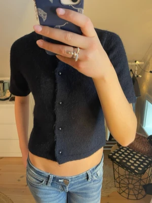 Mörkblå kofta från Gina Tricot - Kortärmad bli stickad kofta med pärl knappar från Gina Young. Jag säljer den då den är för kort och kommer för av inte till användning!! Använd endast ett få tal gånger och därför ingen defekt på plagget!🩷