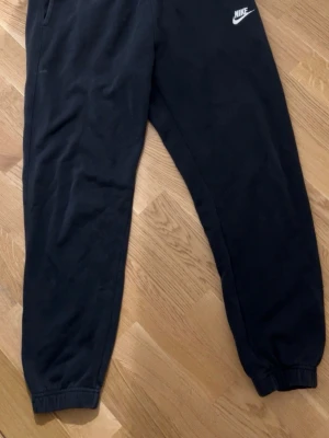 Svarta mjukisbyxor från Nike M - Svarta mjukisbyxor från Nike i storlek M. Byxorna har resår i midjan och vid bensluten, sidofickor och en bakficka. Klassisk Nike-logga broderad framtill. Perfekta för chill eller träning.