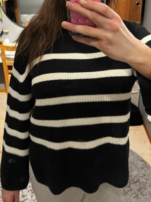 Svart vit randig stickad tröja från Kappahl  - Fin stickad svartvit tröja från Kappahl med en liten polokrage. Den är tjock och perfekt nu i vintern. Den har två jack på sidan för att göra den mer luftig.