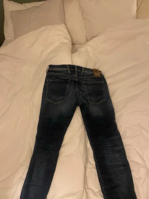 Replay Anbass blå jeans, storlek 31 - Säljer ett par Replay Anbass jeans i klassisk blå tvätt med snygga slitningar och kontrastsömmar. Jeansen har normal (lite åt skinny sidan) passform och raka ben. Märkespatch bak i midjan och Replay-detaljer på fickan fram. Perfekta för dig som gillar stilrena och bekväma jeans. Vid minsta fundering hör av dig, pris går att förhandla. 