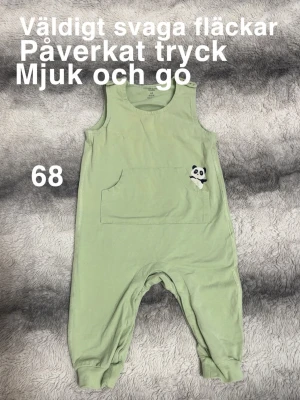 Gröna byxdress med panda-detalj - Söt ljusgrön byxdress för baby med stor ficka framtill och en liten panda-applikation. Ärmlös modell, perfekt för lek och mysiga dagar. Smidiga tryckknappar på axlarna för enkel påklädning.🌸 Väldigt svaga fläckar. Påverkat tryck. Mjuka och sköna. Storlek 68
