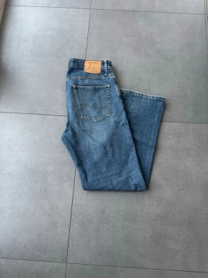 Loose/Eddie blå jeans 30/32 - Säljer ett par klassiska blå jeans från Loose/Eddie i storlek 30/32. Jeansen har en loose passform med raka ben och femficksmodell. Tillverkade i slitstarkt denimtyg med snygga kontrastsömmar och en enkel bakficka.