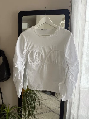 Vit långärmad topp  - Säljer en vit långärmad topp med unika detaljer över bysten och längs ärmarna. Toppen har rund halsringning och är gjord i ett mjukt bomullstyg. Perfekt för dig som gillar en enkel men ändå speciell look.