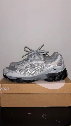 Silverfärgade Asics sneakers - Säljer ett par snygga Asics sneakers i silver och grått med svarta detaljer på sulan. Skorna har meshpaneler för extra ventilation, klassisk snörning och en rund tå. Perfekt för dig som gillar sportig stil och vill ha bekväma skor med cool design.