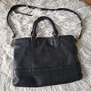 Svart handväska från Tiger of Sweden - Tiger of Sweden Handväska i modellen Florina. Svart läder med guld detaljer. Nypris ca 3595:-  Rymlig handväska i mjukt läder  Många praktiska fack Den har även Tiger of Sweden loggan på framsidan. Stort huvudfack med dragkedja där man fär plats med t.ex dator mm - Fasta bärhandtag - Löstagbar och justerbar axelrem - 2 fack med magnetknapp - 1 invändigt fack med dragkedja - 2 invändiga öppnafack 42x30cm  Mycket bra skick men finns tecken på användning, skriv för detaljer. 