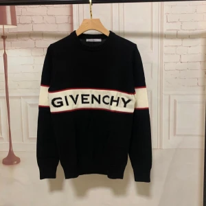 Svart stickad tröja från Givenchy - Svart stickad tröja från Givenchy med vit panel och röd kant över bröstet där loggan är broderad i svart. Tröjan har rund hals, ribbade muddar och lång ärm. Materialet är mjukt och grovstickat, perfekt för att hålla värmen. Snygg kontrast mellan färgerna och stilren design.