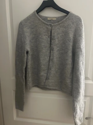 Grå kofta från gina - Mysig grå kofta från gina med rund hals och knappar framtill. Den är stickad i mjukt material och har långa ärmar. Enkel och stilren design som funkar till det mesta.