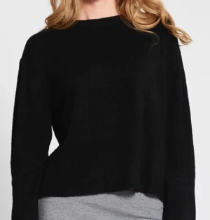 Svart stickad tröja med lång ärm - En svart stickad tröja med rund hals och lång ärm. Modellen är lite croppad och har en enkel, clean look som passar till jeans eller kjol. Mjuk och skön känsla, perfekt för kyliga dagar. Snygg att styla med lager på lager.