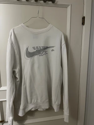 Vit Nike sweatshirt  - Vit sweatshirt från Nike i storlek M med stort Swoosh-tryck och text på bröstet. Tröjan har rund hals, långa ärmar och är gjord i mjuk bomullsmix. Perfekt för dig som gillar clean och sportig stil med tydlig logga framtill.
