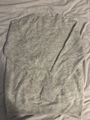 Kashmir tröja  - En enkel och stilren ljusgrå stickad tröja med rund hals och långa ärmar. Tröjan har ribbade muddar vid ärmslut och nederkant, vilket ger en snygg och bekväm passform. Perfekt för lager-på-lager under kyliga dagar.