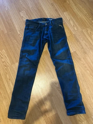 Replay blå jeans straight fit - Snygga blå jeans från Replay med klassisk femficksdesign och raka ben. Jeansen har en mörk tvätt med lätt slitning och kontrastsömmar. Passar dig som gillar en stilren look med bekväm passform. Materialet är mjukt jeans och midjan är normal.