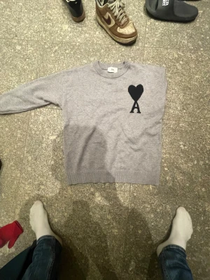 Ami pris knitt, kofta - Snygg grå stickad tröja från Ami med svart hjärta och A på bröstet. Tröjan har rund hals, ribbade muddar och är långärmad. Jag har ärvt denna av en släkting som inte fått någon användning för den. Den är tyvärr lite för liten för mig men i princip helt oanvänd. Bara att fråga om det skulle vara något pris går att diskutera…