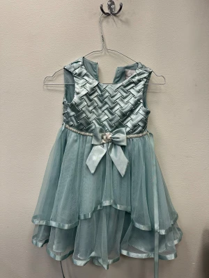 Ljusblå kortklänning med rosett - Superfin ljusblå kortklänning med flätad satin upptill och lager av tunn tyll i kjolen. Klänningen har pärldetaljer i midjan och en stor rosett framtill med en liten blomma. Ärmlös modell med dragkedja i ryggen och glansiga kantband på kjolen.