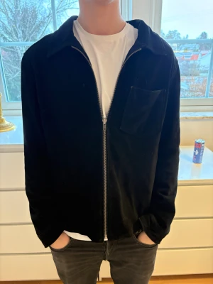 Svart manchesterjacka från MDK - Säljer en svart manchesterjacka från Munderingskompagniet/MDK. Jackan har en clean look med rak passform, bröstficka och dragkedja framtill. Perfekt för dig som gillar stilrena och tidlösa plagg. Passar till det mesta och är riktigt skön att bära.