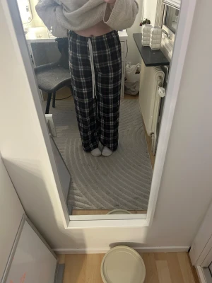 Rutig mjukisbyxa med snörning - Mysiga mjukisbyxor i rött, vitt och mörkblått rutmönster. Vida ben och hög midja med vit snörning i midjan. Tillverkade i mjukt bomullstyg, perfekta för chill dagar hemma.