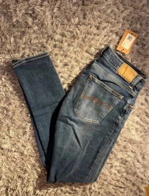 Blåa Nudie Jeans  - Snygga blå jeans från Nudie Jeans med klassisk femficksdesign och kontrastsömmar. Modellen har rak passform och normal midja, tillverkade i slitstark bomull. Perfekt för dig som gillar stilrena och tidlösa jeans med cool tvätt. Storleken är 31/36 men sitter som 32-34 i längd. Måttet på längden är 104cm