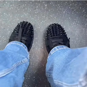 Christian Louboutin svarta sneakers med nitar - Svarta sneakers från Christian Louboutin med glittrig yta och svarta nitar över tå och häl. Skorna har snörning och platt sula, samt den ikoniska röda undersidan. Perfekt för dig som vill sticka ut med edgy och lyxig stil. Fick dem i 18 års present.