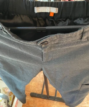 Svarta byxor från Homebound, stl S - Svarta byxor från Homebound i storlek S. Byxorna har resår i midjan för extra komfort och är tillverkade i ett mjukt, slätt material med diskret glans. Klassisk passform med knapp och hällor för bälte. Perfekta för en clean och stilren look. Insydda lite slarvigt och välanvända.