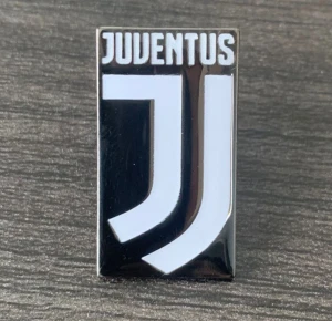 Juventus pin i svart och vitt - Juventus pin med klubbens moderna logga i svart och vitt. Rektangulär form med tydlig text och stilren design, perfekt för att visa ditt stöd för laget. Passar att fästa på jacka, väska eller keps för en sportig vibe.