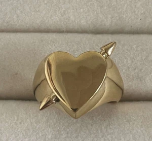 Guldfärgad ring med hjärtdetalj - Cool ring i guldfärg med ett stort hjärta i mitten och två spetsiga detaljer på sidorna. Ringen har en chunky design som verkligen sticker ut och passar dig som gillar statement-smycken. Perfekt att matcha med andra guldsmycken för en unik look. Rostfri