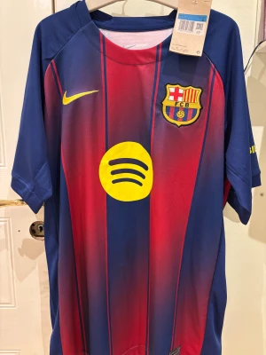 FC Barcelona Lamine Yamal matchtröja - Säljer en officiell FC Barcelona matchtröja från Nike med Lamine Yamal och nummer 10 på ryggen. Tröjan är blå och röd med gula detaljer, randigt mönster, klubbmärke, Spotify-logga och Champions League-patch på ärmen. Tillverkad i lätt och ventilerande polyester.