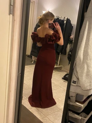 Vinröd långklänning  - Säljer en vinröd långklänning med offshoulder och stora volanger runt axlarna. Har en hög slits på ena sidan. (OBS, slitsen är igen syd men det gör att sprätta)🥰 Använd 1 gång! Nypris:1800 