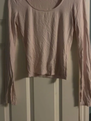 Ljusrosa långärmad topp - En enkel och stilren ljusrosa topp med lång ärm och rundad halsringning. Tillverkad i mjukt bomullsmaterial som känns skönt mot huden. Perfekt att matcha med jeans eller kjol för en clean look.