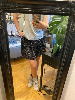 Svart volangkjol med vita prickar - Supersöt svart kortkjol med vita prickar och dubbla volanger. Kjolen har en flowy passform och elastisk midja som gör den bekväm och enkel att bära. Det går att bestämma ifall ma vill ha låg eller hög midja. Supersöt på sommaren!!