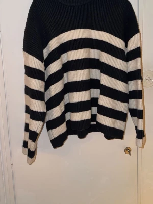 Randig stickad tröja från Monki XL - Säljer en oversized stickad tröja från Monki i svart och vitt med breda ränder. Tröjan har lång ärm och ribbad struktur, perfekt för dig som gillar en chill och trendig look. Materialet är en mix av akryl, polyamid och lite ull.