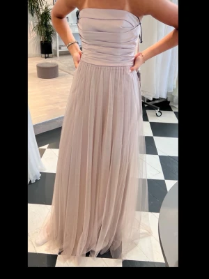 Ljusbeige balklänning - Säljer min balklänning i ljusbeige ton med flera lager mjuk tyll som ger ett drömmigt och flytande intryck. Klänningen har en markerad midja och ett svepande fall, perfekt för bal. Skulle säga att den passar både storlek s och m