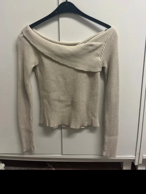 Beige ribbad offshoulder stickad tröja - Säljer en beige ribbad stickad tröja med offshoulder-design och långa ärmar. Tröjan har en bred krage som vilar snyggt över axlarna och ger en trendig look. Perfekt för dig som gillar stilrena och bekväma plagg med lite edge. Se bild 2 för defekt kan sys ihop men även användas så då det ej är märkbart!