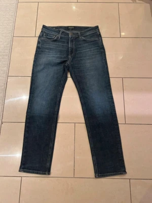 Mörkblå jeans Regular/Clark Jack and Jones  - Snygga mörkblå jeans från Jack and Jones modell: Regular/Clark med klassisk femficksdesign och raka ben. Jeansen har en diskret tvättad look och kontrastsömmar. Perfekta till vardags och passar till det mesta. Materialet är slitstarkt jeans i bomull.