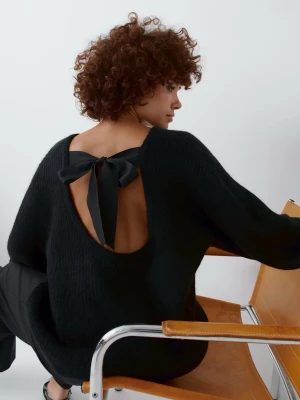 Svart stickad tröja med rosett i ryggen - Svart stickad tröja med öppen rygg och stor rosett som knyts i nacken. Tröjan har lång ärm och en loose passform, perfekt för dig som vill ha något både snyggt och bekvämt. Materialet är mjukt och ger en mysig känsla.