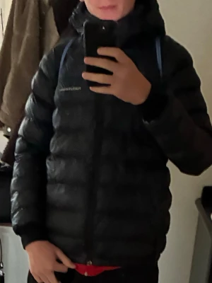 Svart dunjacka från Peak Performance - Säljer en svart dunjacka från Peak Performance med huva och dragkedja framtill. Jackan har en puffig design och är perfekt för kalla dagar. Enkel och stilren look som funkar till det mesta. Hör av dig vid frågor! Storlek 170-175