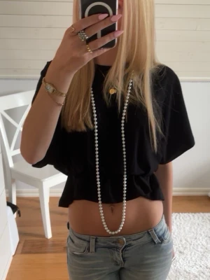 Svart croppad topp med kort ärm - Säljer en svart croppad topp med korta ärmar och rund hals. Toppen har en lös passform och resår i midjan som ger en snygg siluett. Perfekt att matcha med jeans eller kjol för en trendig look.