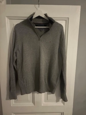 Grå half zip tröja Tommy Hilfiger - Snygg grå långärmad tröja från Tommy Hilfiger med ribbade muddar och krage. Klassisk half zip-dragkedja och liten logga på bröstet. Perfekt till lager på lager och funkar året runt.
