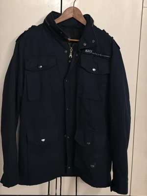 Svart parkajacka från Black Premium - Säljer en svart parkajacka från Black Premium by EMP. Jackan har flera stora fickor med lock och knappar, axelklaffar och dragkedja framtill. Stilen är clean och funktionell, perfekt för dig som gillar streetwear och vill ha en jacka med mycket detaljer.