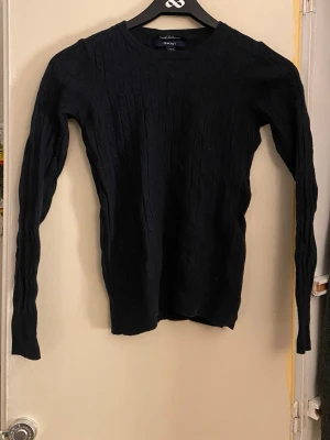 Mörkblå kabelstickad tröja från Gant - Säljer en mörkblå kabelstickad tröja från Gant med diskret broderad logga på bröstet. Tröjan har rund halsringning och långa ärmar. Perfekt till höst och vinter för en clean och klassisk look.